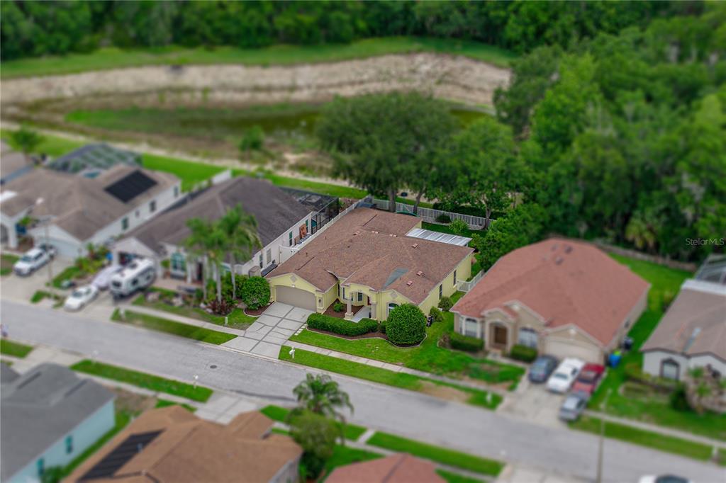 An aerial view shows a yellow suburban house with a brown roof and a pool — 1808 TANGLEDVINE DRIVE, WESLEY CHAPEL, FL