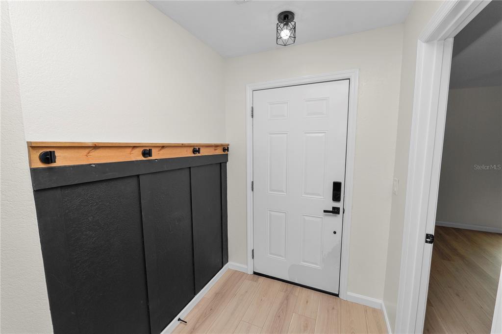 An entryway features light wood flooring, a white door, and a black board-and-batten accent wall — 3664 WILLOW WISP DRIVE S, LAKELAND, FL