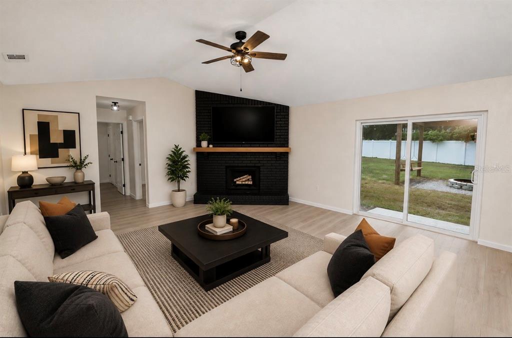 A living room features a black brick corner fireplace, light flooring, and a sliding glass door — 3664 WILLOW WISP DRIVE S, LAKELAND, FL