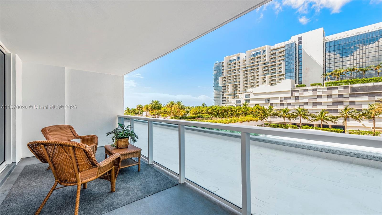 A balcony features two wicker chairs, a small side table, and a glass railing — 2301 Collins Ave # 301, Miami Beach FL 33139, MIAMI BEACH, FL