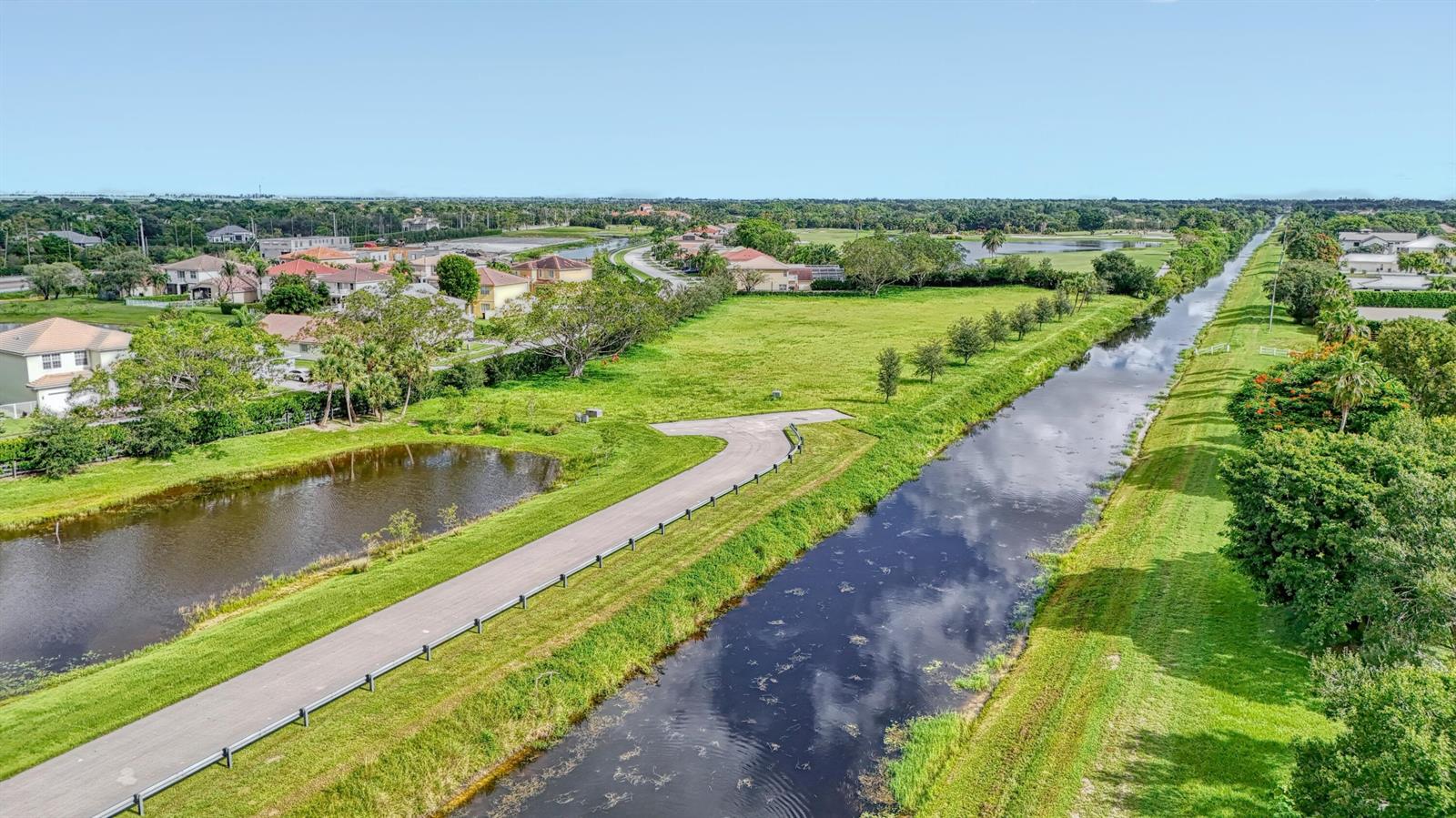 An aerial view shows a canal running alongside a paved path and residential houses — 3102 Greenbriar Boulevard, Wellington FL 33414, WELLINGTON, FL