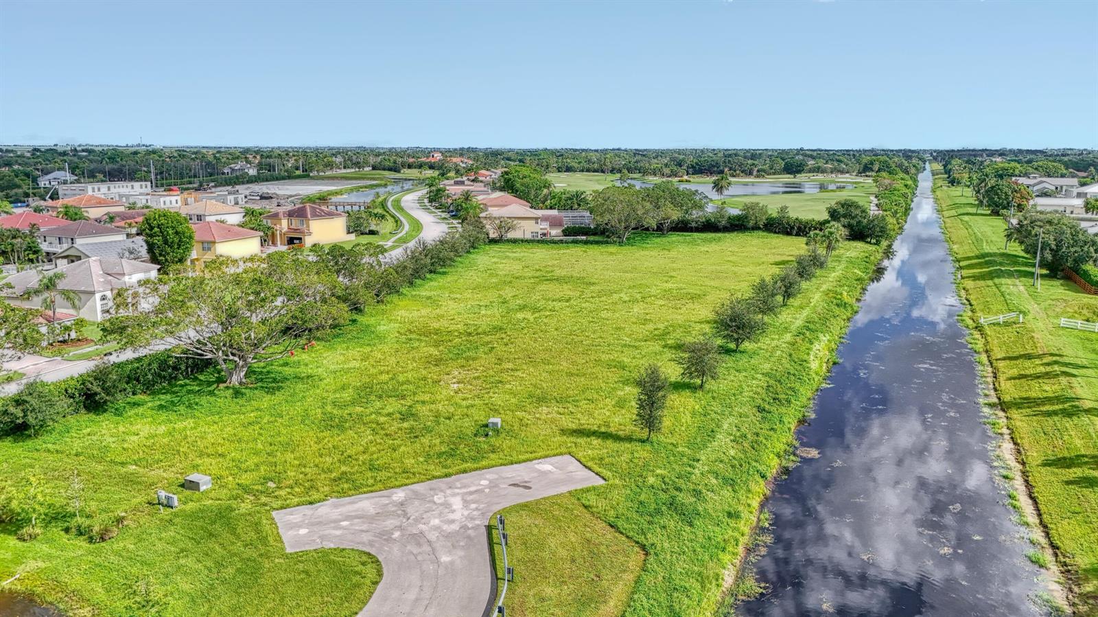 An aerial view shows a vacant grassy lot bordered by a canal and residential houses — 3102 Greenbriar Boulevard, Wellington FL 33414, WELLINGTON, FL