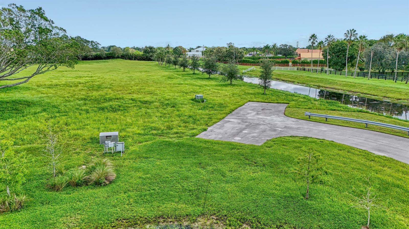 An aerial view shows a large, grassy lot with a concrete driveway and a canal — 3102 Greenbriar Boulevard, Wellington FL 33414, WELLINGTON, FL