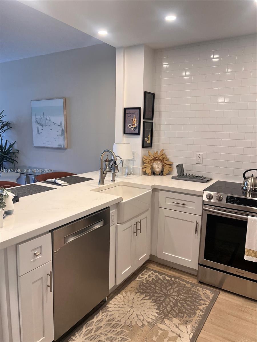 A modern kitchen features white cabinets, a farmhouse sink, stainless steel appliances, and subway tile — 400 N Riverside Dr # 410, Pompano Beach FL 33062, POMPANO BEACH, FL
