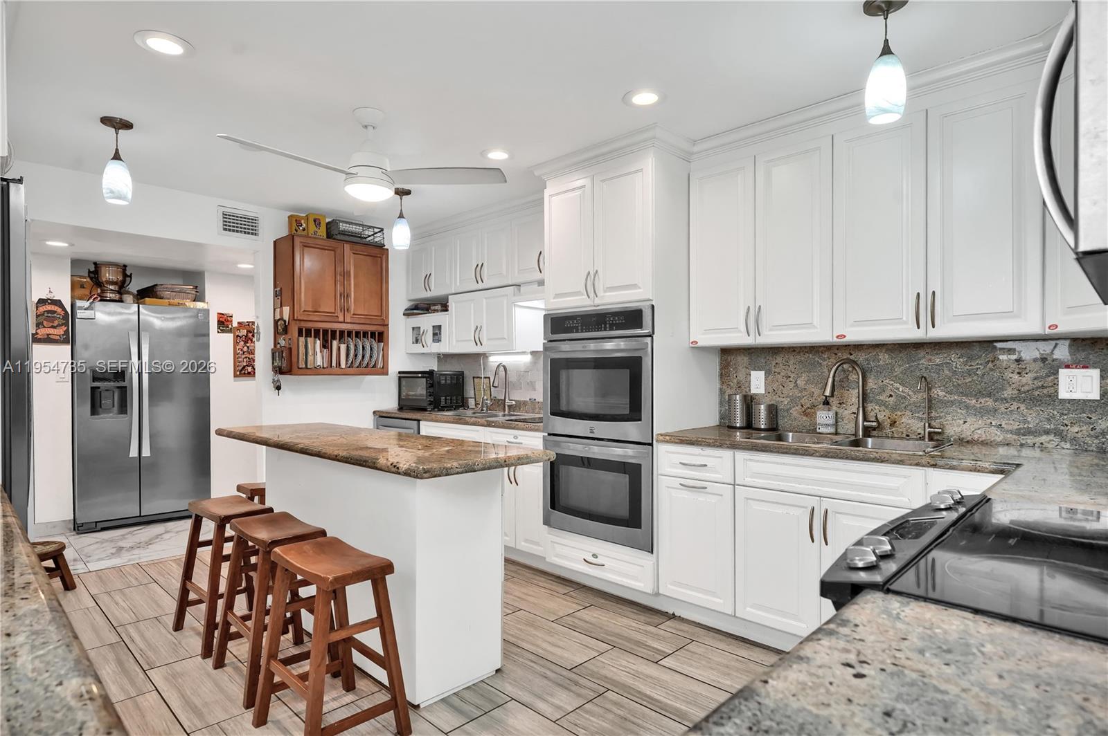 A kitchen features white cabinets, granite countertops, stainless steel appliances, and a wooden breakfast island — 16750 NE 10th Ave, North Miami Beach FL 33162, NORTH MIAMI BEACH, FL
