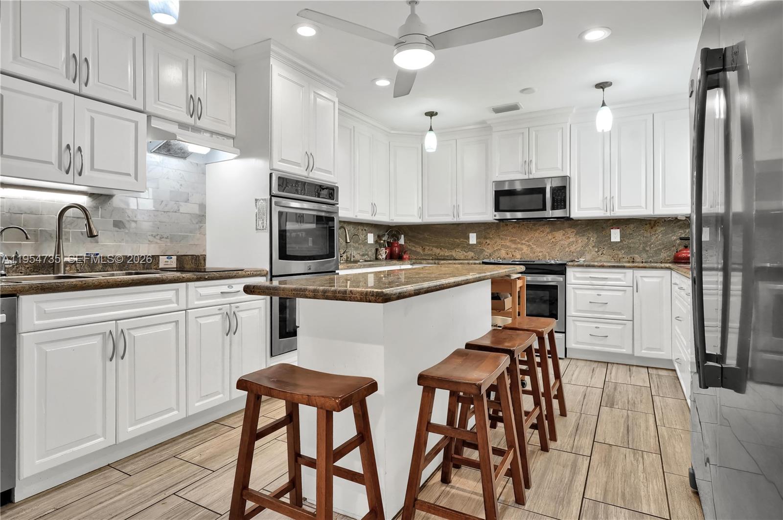 A kitchen features white cabinetry, granite countertops, stainless steel appliances, and a central island — 16750 NE 10th Ave, North Miami Beach FL 33162, NORTH MIAMI BEACH, FL