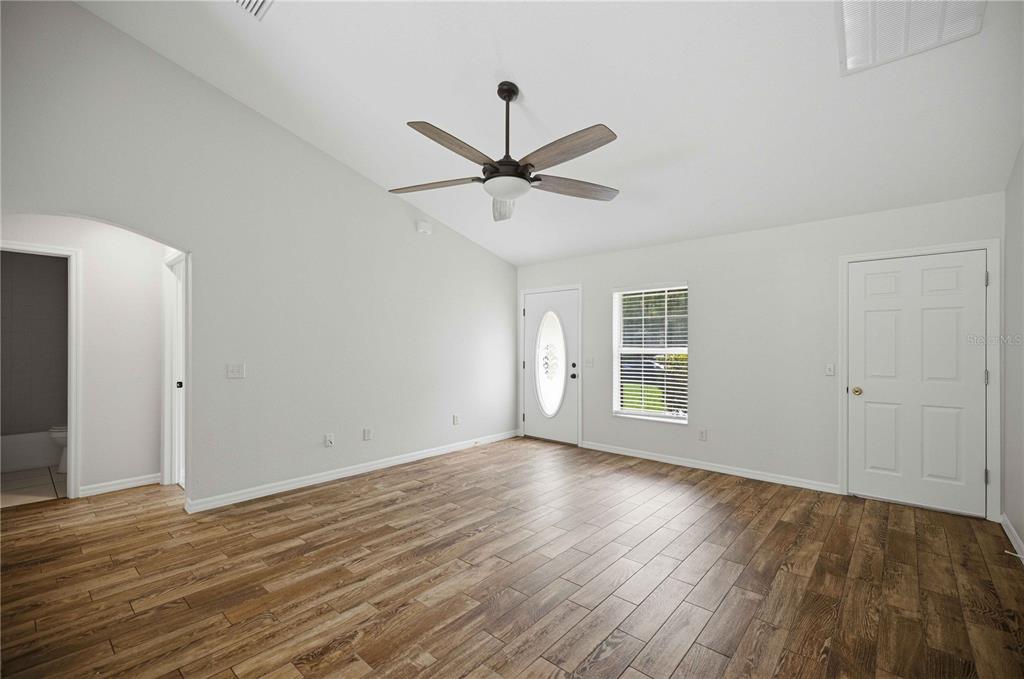 An empty room with wood-look tile flooring, a vaulted ceiling, a ceiling fan, and two doors — 5522 NW 60TH TERRACE, OCALA, FL