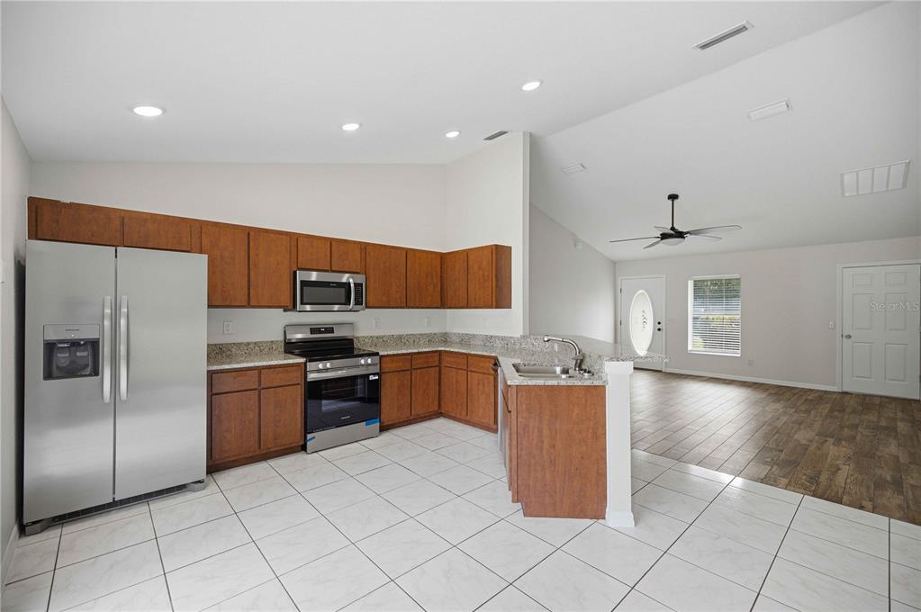A kitchen with wood cabinets, stainless steel appliances, and tile flooring opens to a living area — 5522 NW 60TH TERRACE, OCALA, FL