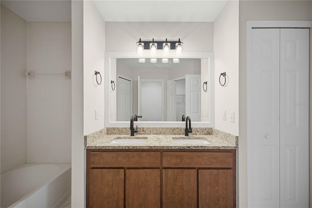 A bathroom features a double-sink vanity with a granite countertop, dark wood cabinets, and mirrors — 5522 NW 60TH TERRACE, OCALA, FL