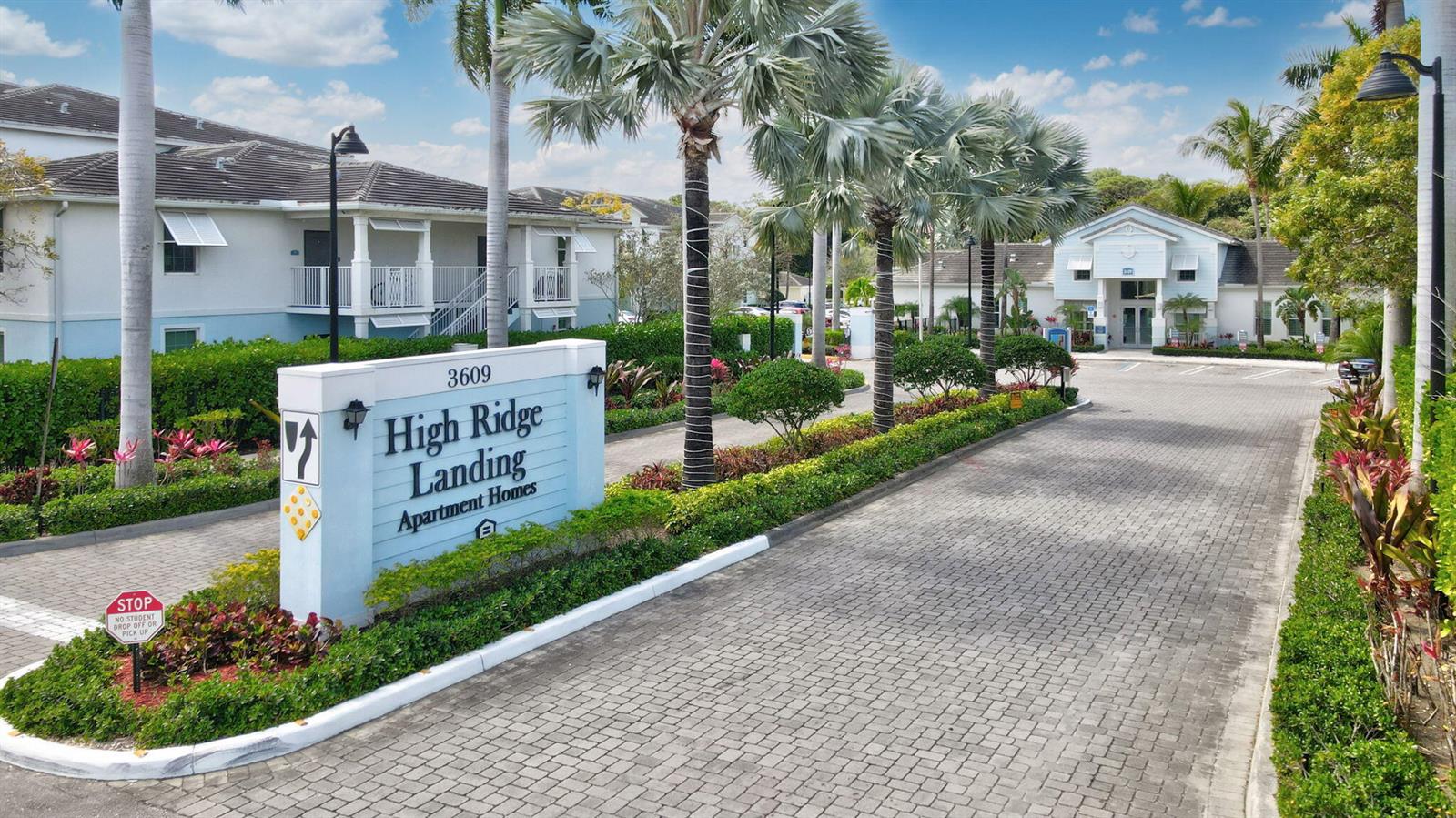 The entrance to an apartment complex features a sign, paved driveway, and palm trees — 3603 High Ridge Way # 302, Boynton Beach FL 33426, BOYNTON BEACH, FL