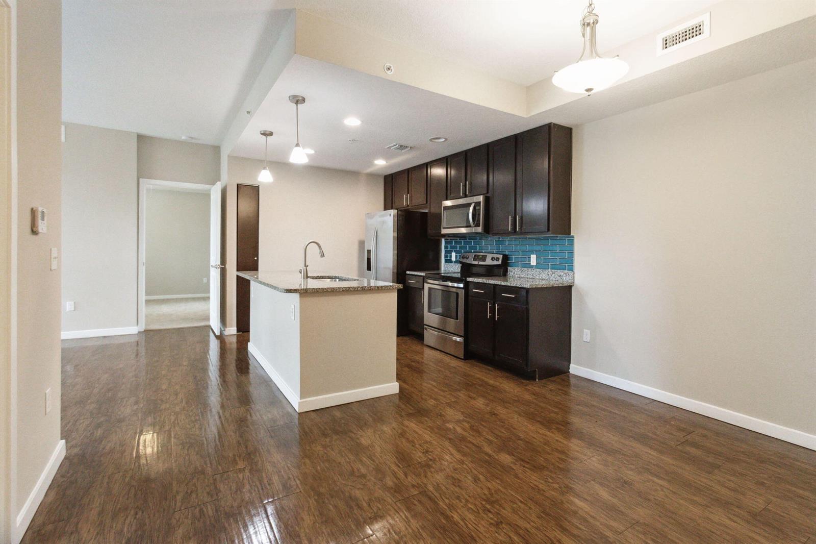 A kitchen with dark cabinets, stainless steel appliances, a granite island, and wood-look flooring — 3603 High Ridge Way # 302, Boynton Beach FL 33426, BOYNTON BEACH, FL