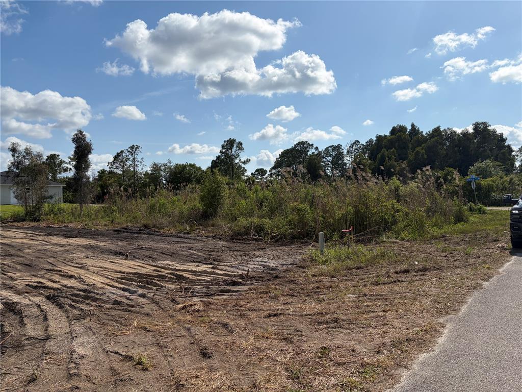 A cleared, dirt-covered residential lot features a nearby house and construction equipment — 2619 26TH STREET W, LEHIGH ACRES, FL