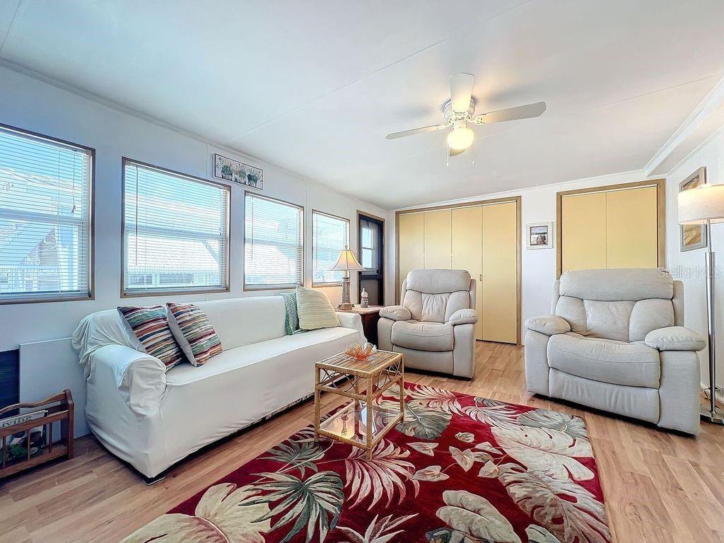 A living room features a white sofa, two recliners, a patterned rug, and wood flooring — 3333 26TH AVENUE E UNIT 1099, BRADENTON, FL