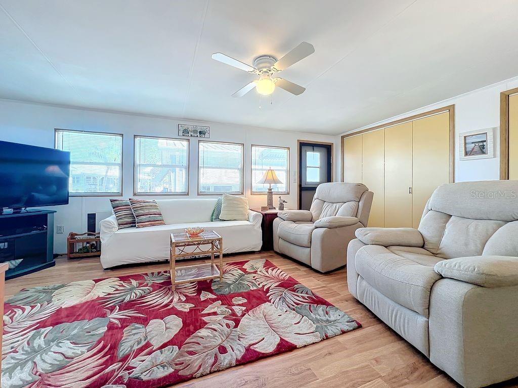 A living room features a tropical-patterned rug, white sofa, two recliners, and light wood flooring — 3333 26TH AVENUE E UNIT 1099, BRADENTON, FL