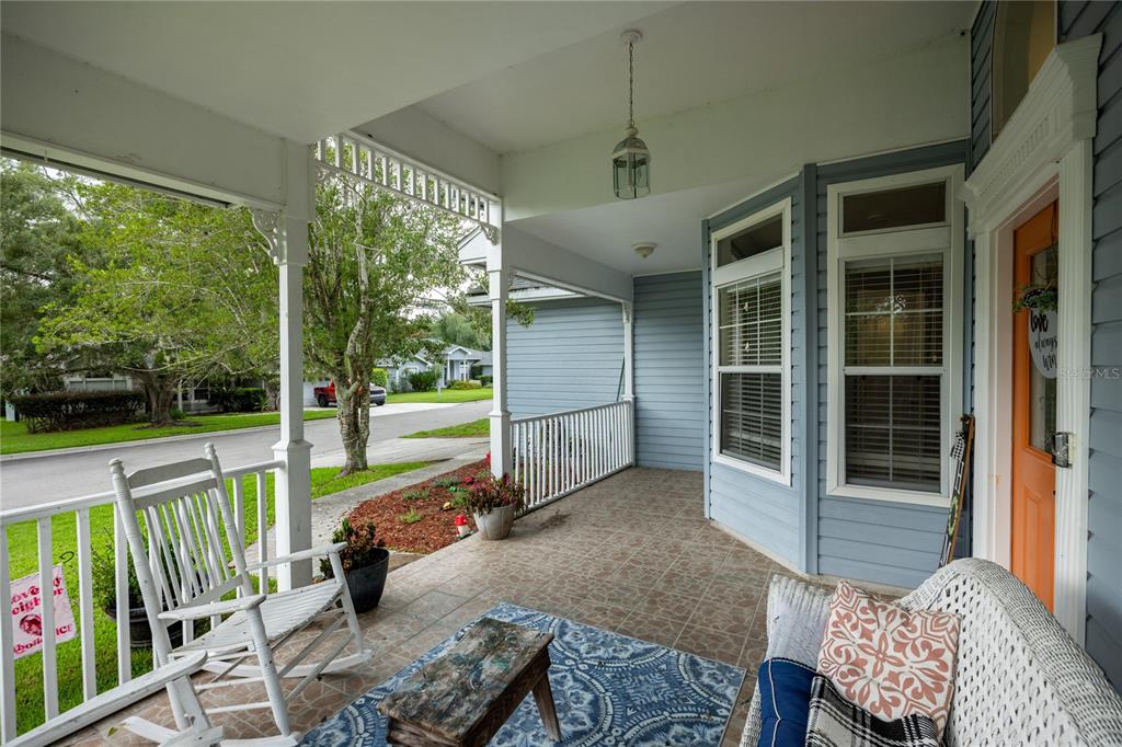 A covered front porch features a white rocking chair, a wicker sofa, and tiled flooring — 11516 NW 16TH PLACE, GAINESVILLE, FL