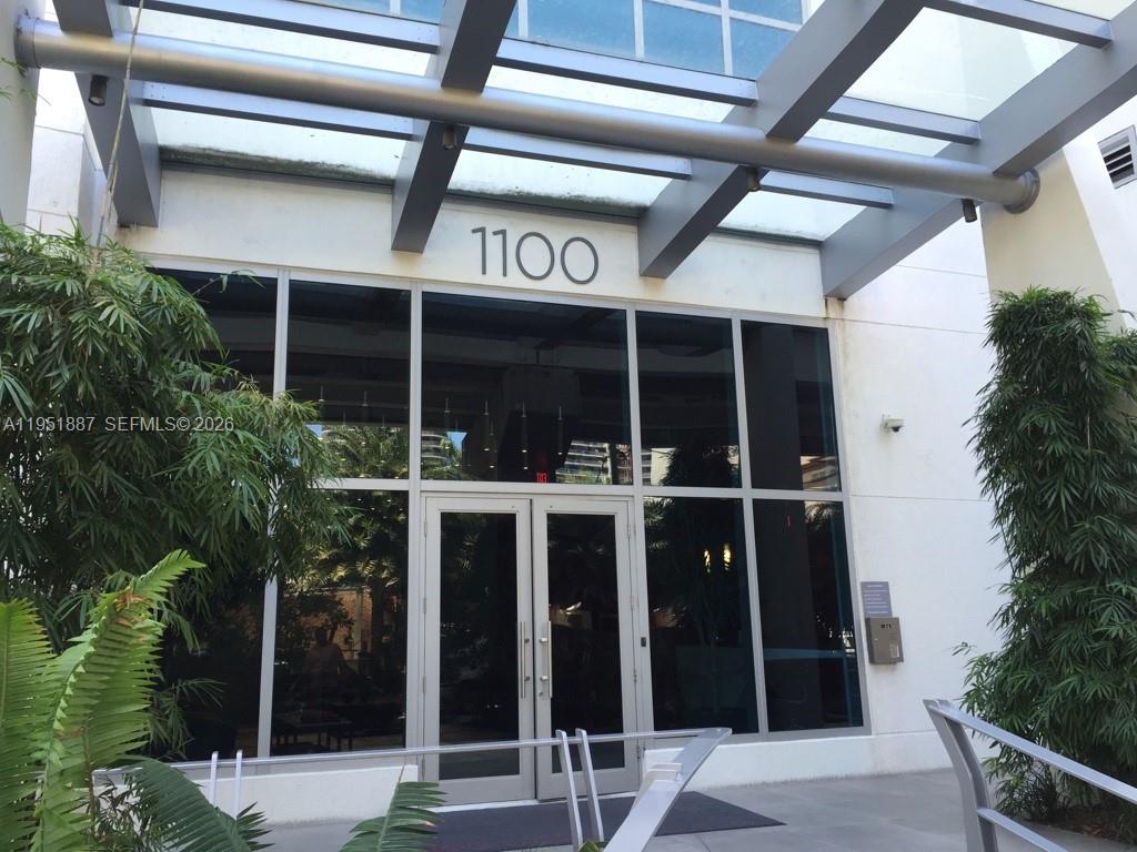 The exterior entrance of a modern building features glass doors under a metal-framed canopy — 1100 S Miami Ave # 2111, Miami FL 33130, MIAMI, FL