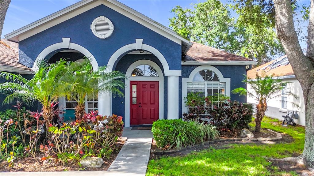 A blue house with a red front door, arched entryways, and landscaping in the front yard — 1904 CATTLEMAN DRIVE, BRANDON, FL