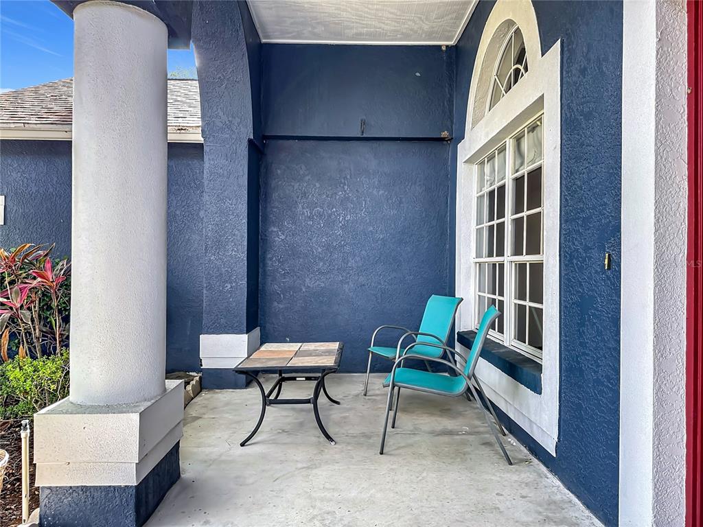 A covered patio features blue stucco walls, a large white column, and two turquoise chairs — 1904 CATTLEMAN DRIVE, BRANDON, FL