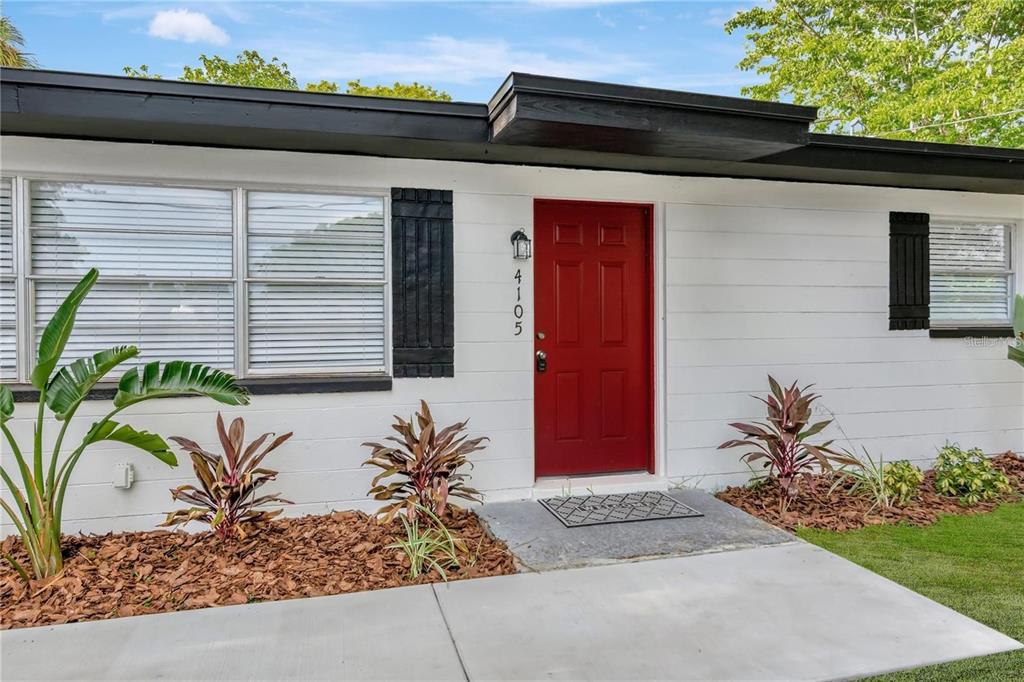 A white house exterior features a bright red front door, black shutters, and landscaped mulch beds — 4105 W MANGO AVENUE, TAMPA, FL