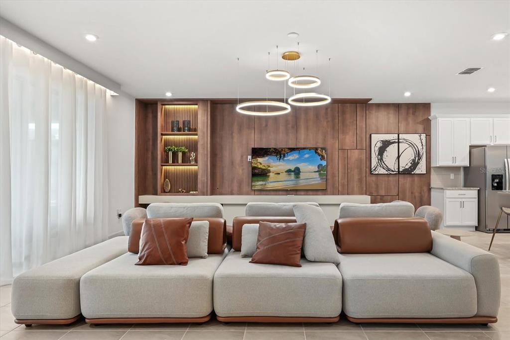 A modern living room features a large modular sofa facing a wood-paneled media wall — 2314 CALM SHORE WAY, KISSIMMEE, FL