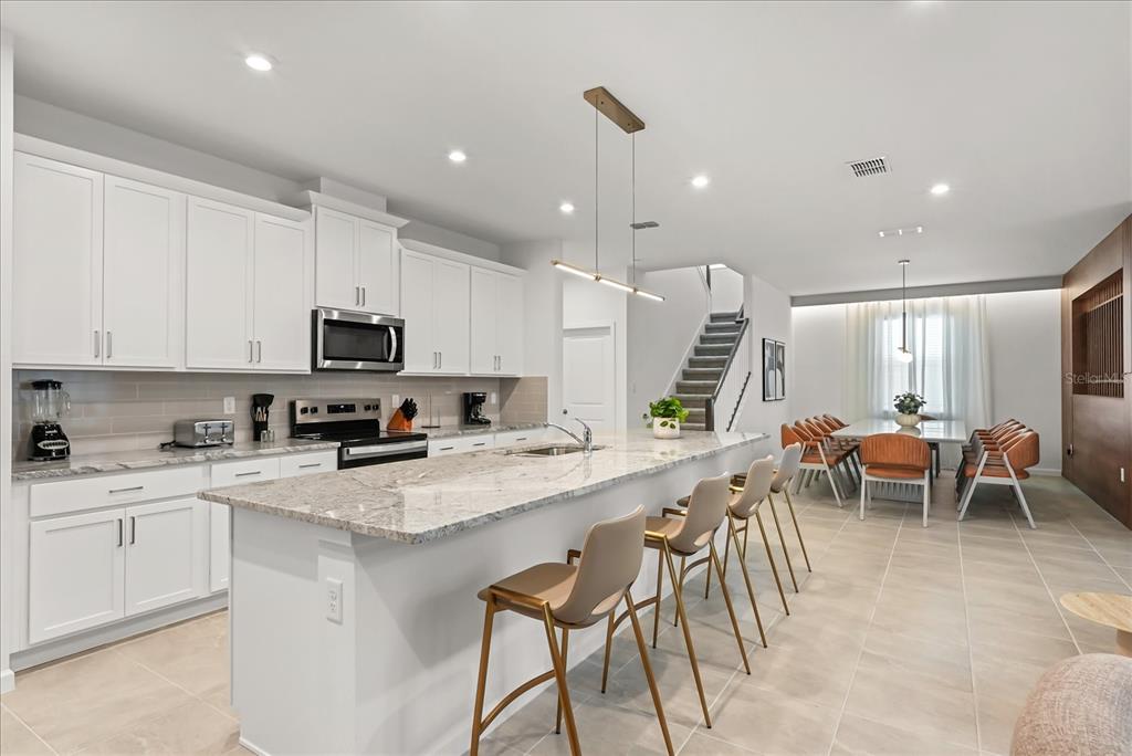 A modern kitchen features white cabinetry, a large granite island, and an adjacent dining area — 2314 CALM SHORE WAY, KISSIMMEE, FL