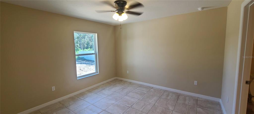An empty bedroom features tan walls, light-colored tile flooring, a ceiling fan, and a window — 3858 SW 133RD LOOP, OCALA, FL