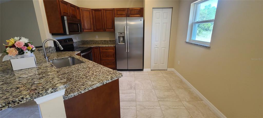A kitchen features wood cabinets, granite countertops, stainless steel appliances, and light-colored floor tiles — 3858 SW 133RD LOOP, OCALA, FL