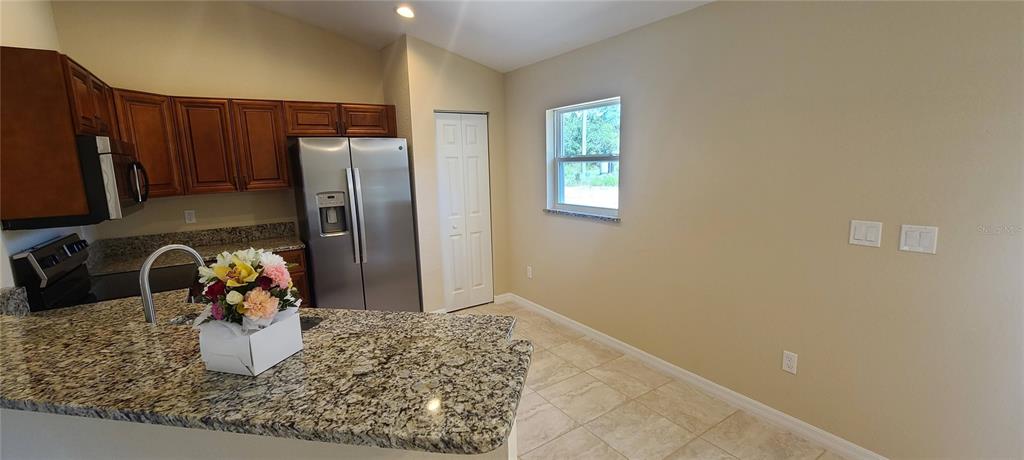 A kitchen features granite countertops, wood cabinets, stainless steel appliances, and tile flooring — 3858 SW 133RD LOOP, OCALA, FL