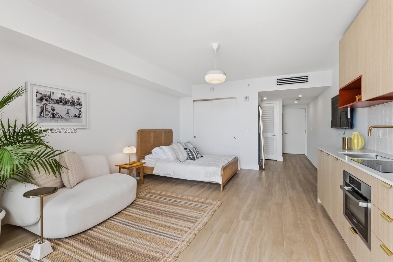 A studio apartment features a bed, sofa, and kitchenette with light wood cabinetry — 90 NE 32ND # 1018, Miami FL 33137, MIAMI, FL