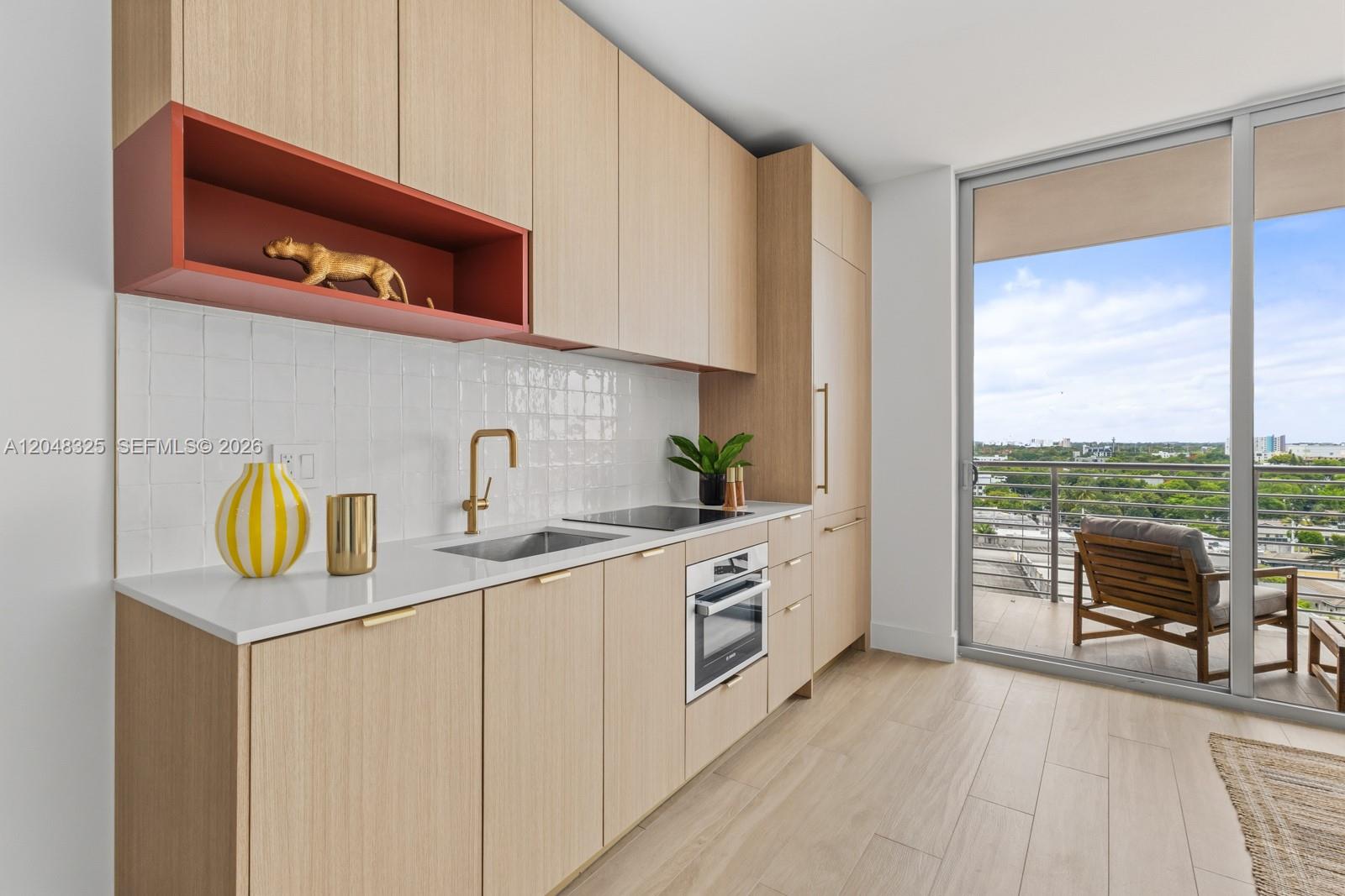 A modern kitchen features light wood cabinets, a red open shelf, and a balcony view — 90 NE 32ND # 1018, Miami FL 33137, MIAMI, FL