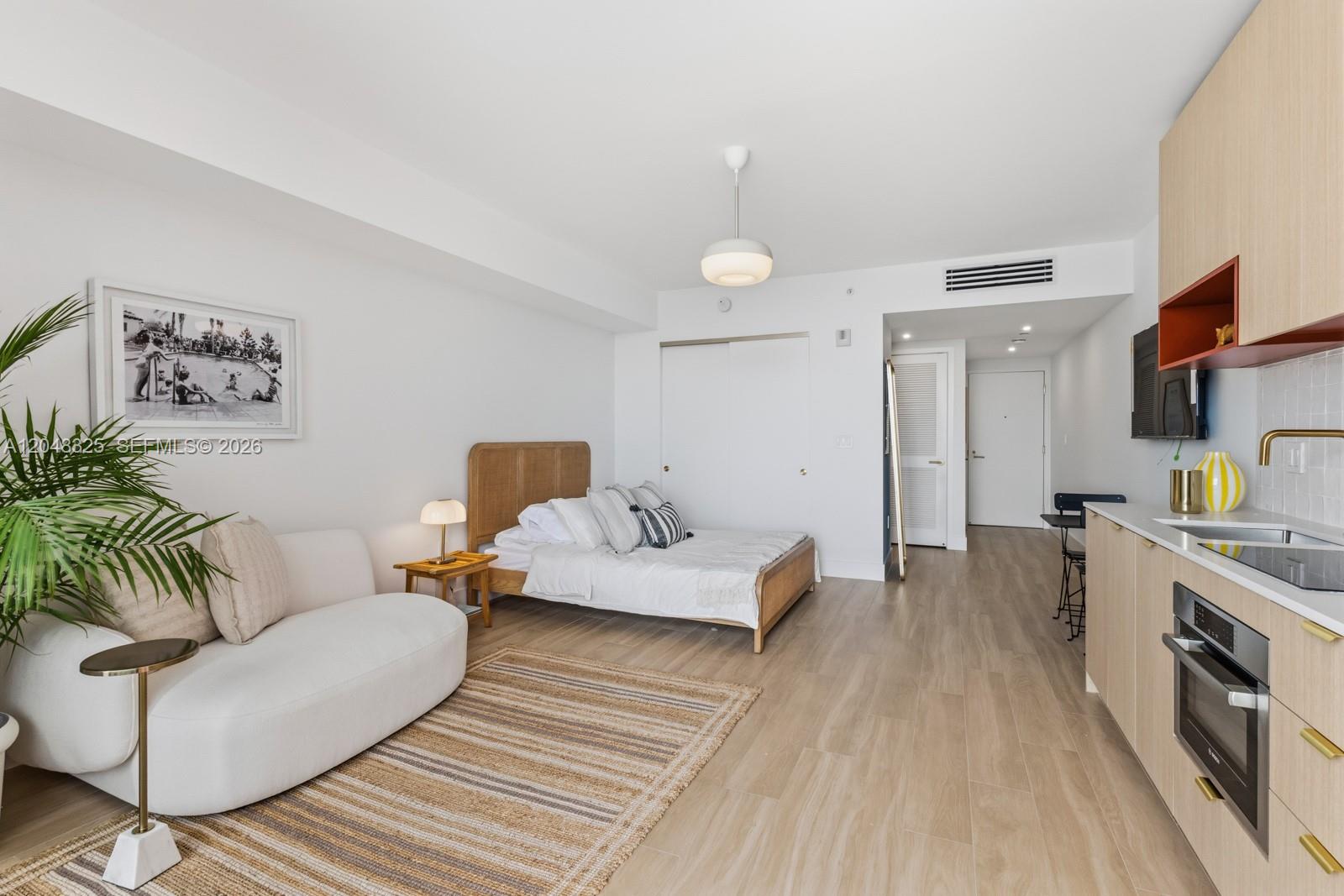 A studio apartment features a bed, a sofa, and a kitchenette with light wood cabinetry — 90 NE 32ND # 1018, Miami FL 33137, MIAMI, FL