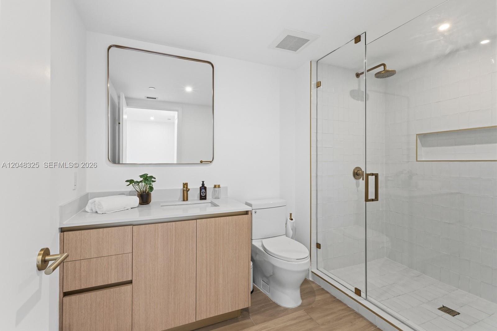 A modern bathroom features a light wood vanity, a glass-enclosed shower, and gold-toned fixtures — 90 NE 32ND # 1018, Miami FL 33137, MIAMI, FL