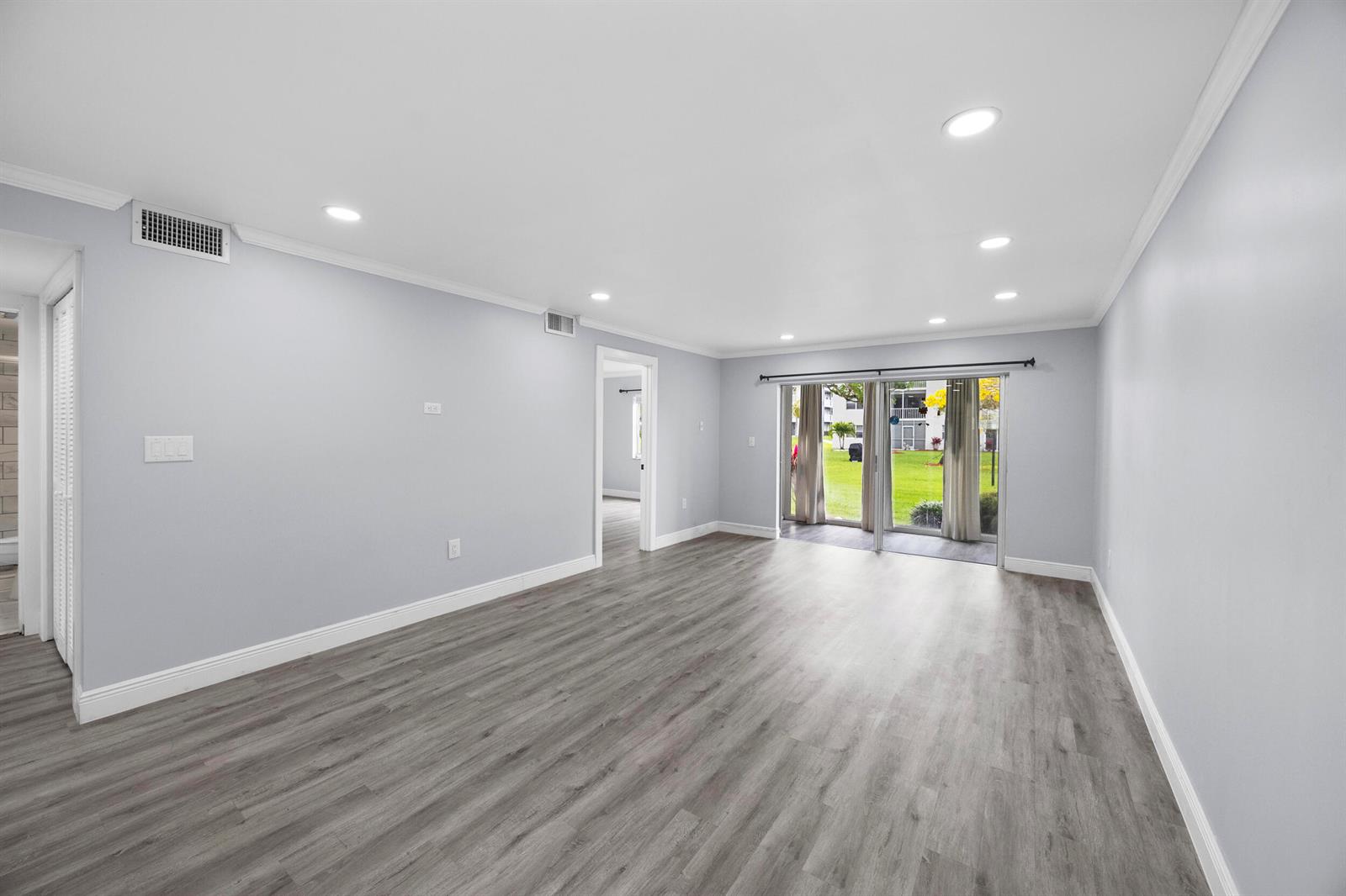 An empty room features light gray walls, wood-look flooring, recessed lighting, and sliding glass doors — 9856 Marina Boulevard # 1314, Boca Raton FL 33428, BOCA RATON, FL