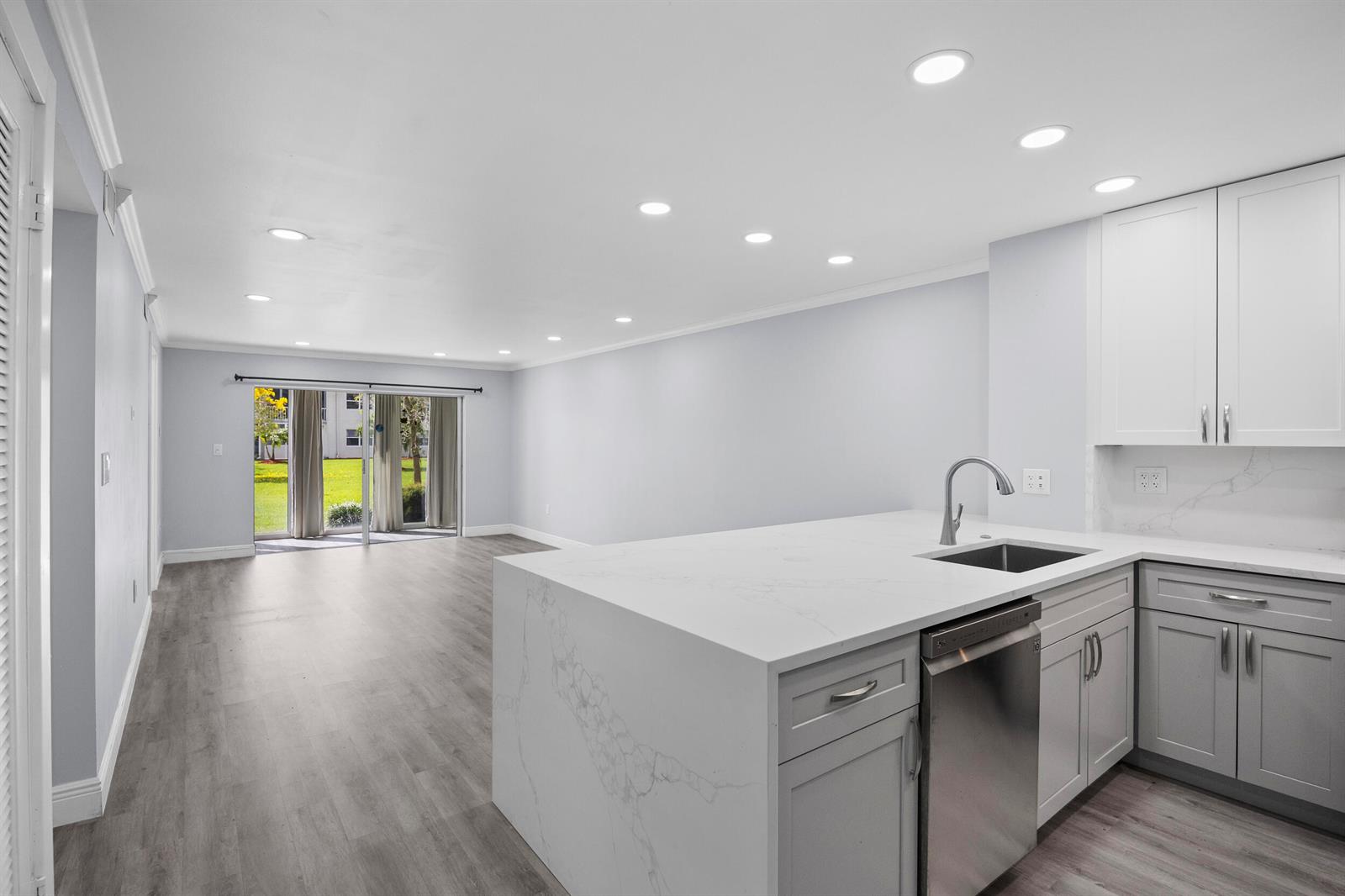 A modern kitchen with a quartz island and gray cabinets opens to a living area — 9856 Marina Boulevard # 1314, Boca Raton FL 33428, BOCA RATON, FL