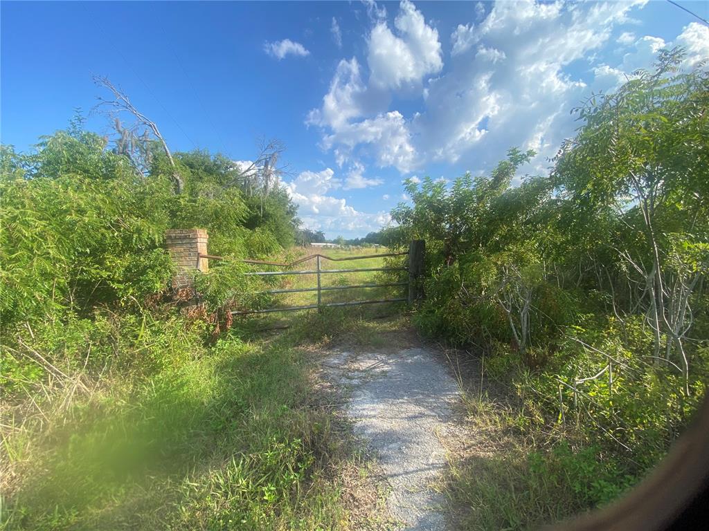 A metal gate stands between a brick pillar and a wooden post on a dirt path — 4210 CARDINAL LANE, KISSIMMEE, FL