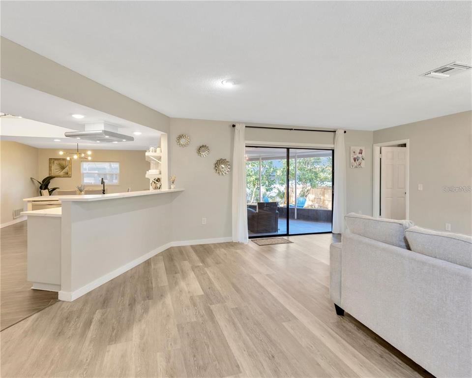 A living room with light wood-look flooring opens to a kitchen and a covered patio — 1414 GULF ROAD, TARPON SPRINGS, FL