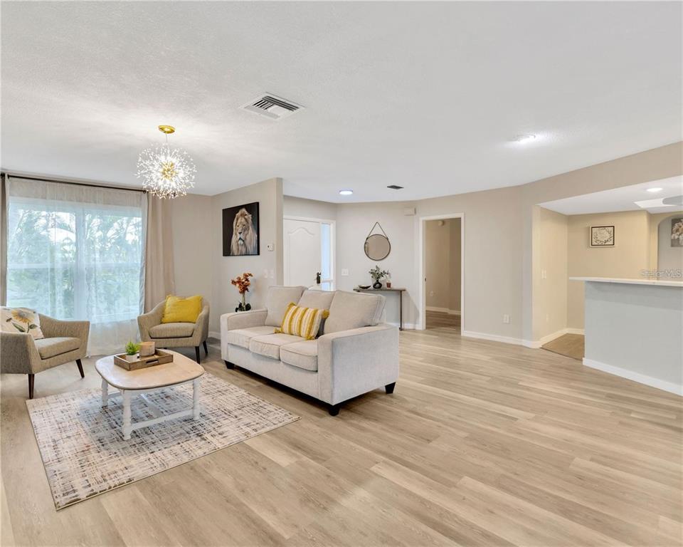 A living room features light wood-look flooring, a neutral sofa, two armchairs, and a chandelier — 1414 GULF ROAD, TARPON SPRINGS, FL