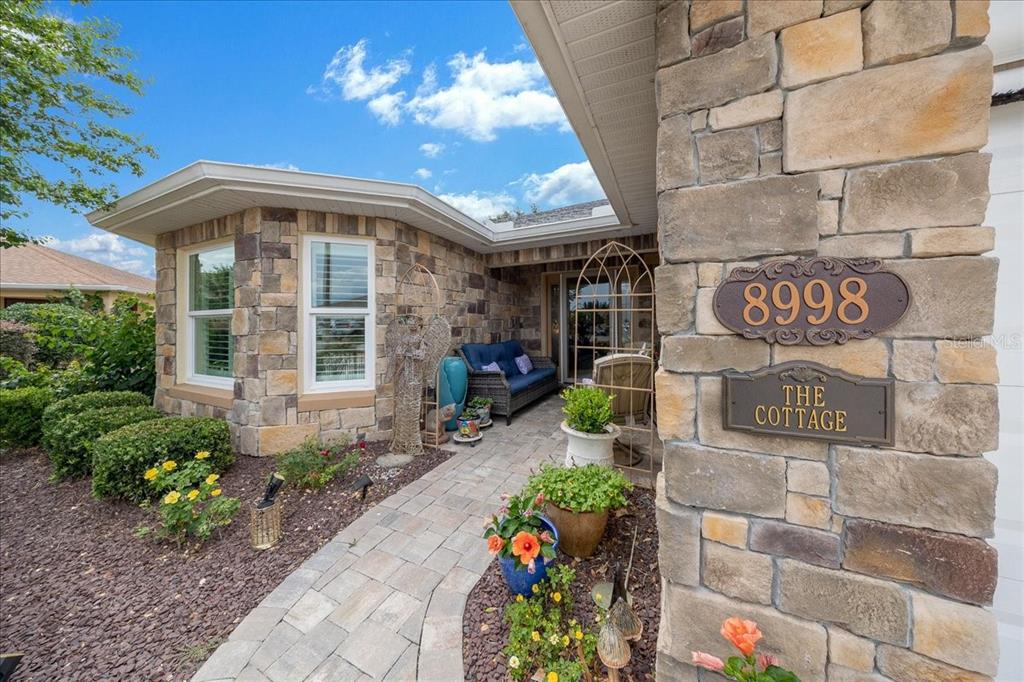 A stone-faced house exterior features a paved walkway leading to a covered entryway with seating — 8998 SW 99TH COURT ROAD, OCALA, FL