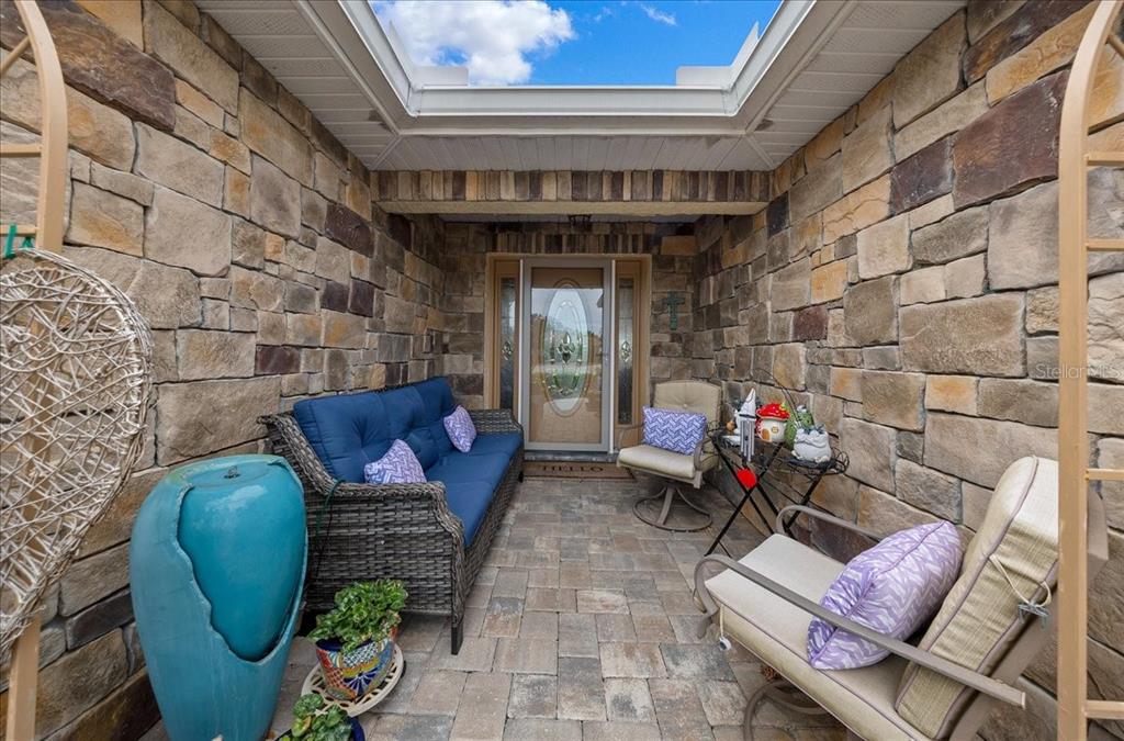 A stone-walled patio features a wicker sofa, two chairs, a fountain, and a skylight — 8998 SW 99TH COURT ROAD, OCALA, FL