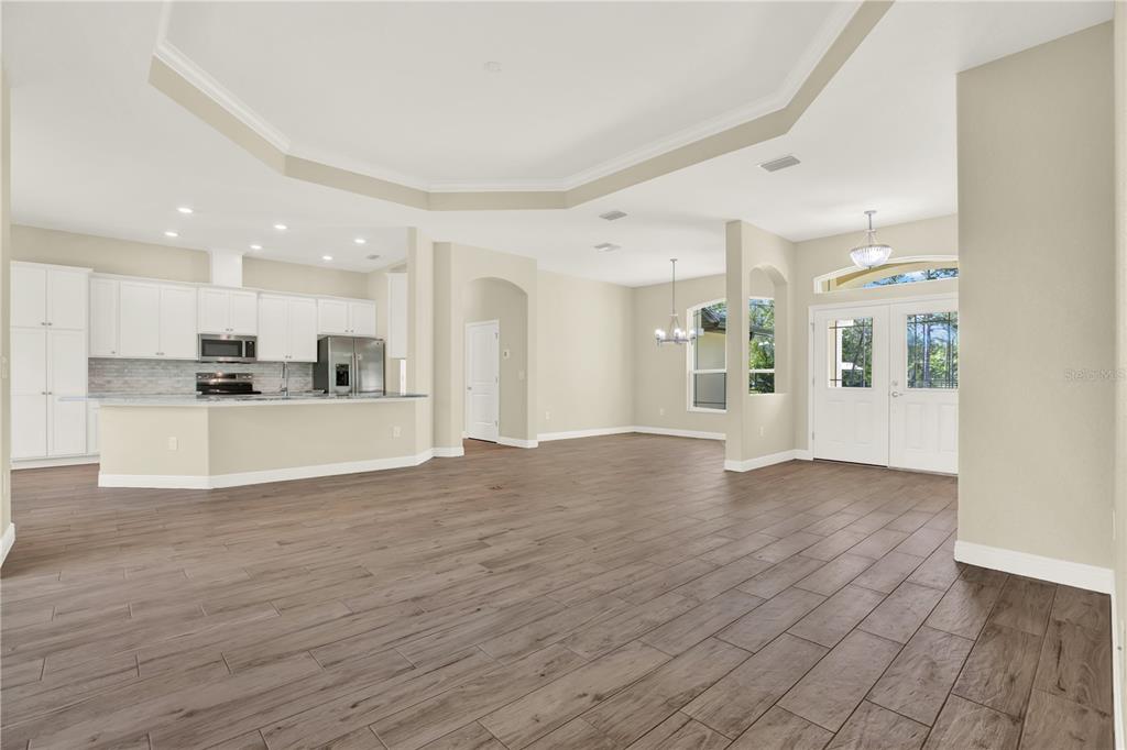 An open-concept living area features a kitchen with white cabinets, wood-look tile flooring, and double-door entry — 12107 HOODED WARBLER COURT, BROOKSVILLE, FL