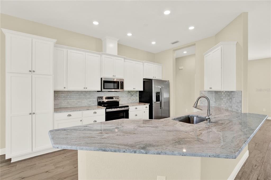 A kitchen features white cabinets, stainless steel appliances, and a granite-topped peninsula with a sink — 12107 HOODED WARBLER COURT, BROOKSVILLE, FL
