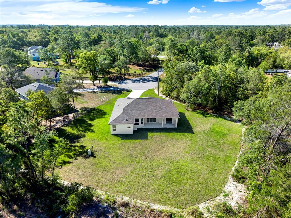 An aerial view shows a single-story house with a large backyard surrounded by trees — 12107 HOODED WARBLER COURT, BROOKSVILLE, FL
