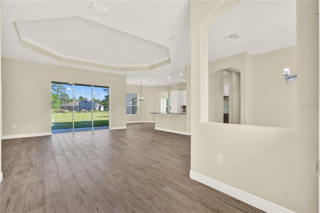 An open-concept living area features wood-look tile flooring, a tray ceiling, and sliding glass doors — 12107 HOODED WARBLER COURT, BROOKSVILLE, FL