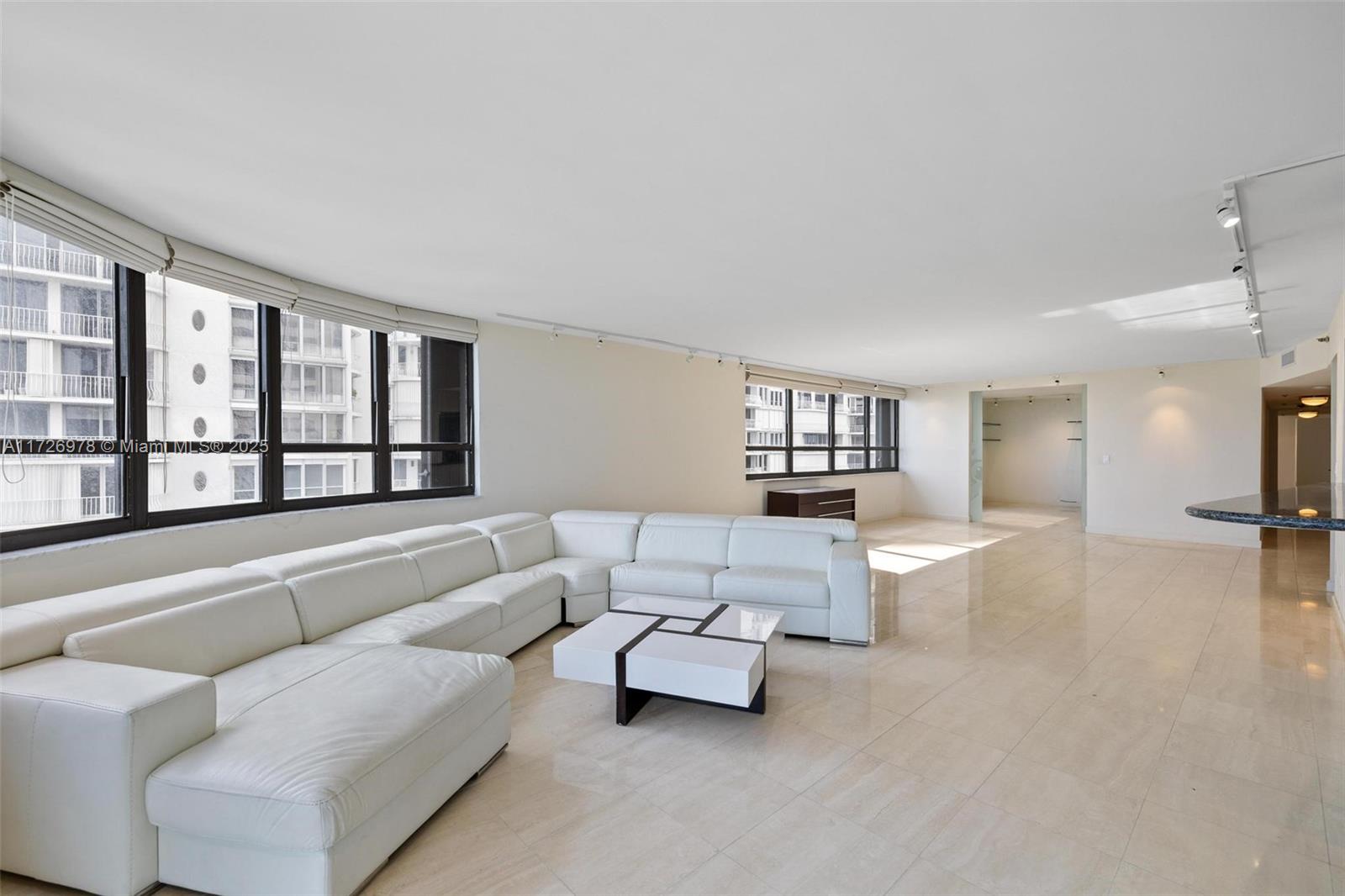 A spacious living room features a white sectional sofa, tile flooring, and large windows — 10175 Collins Ave # 502, Bal Harbour FL 33154, BAL HARBOUR, FL