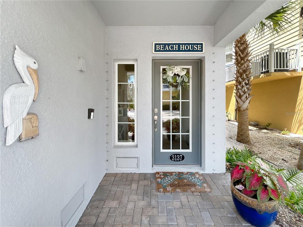 The exterior entrance features a gray door with a wreath, a pelican statue, and pavers — 3137 MOORINGS DRIVE S, ST PETERSBURG, FL