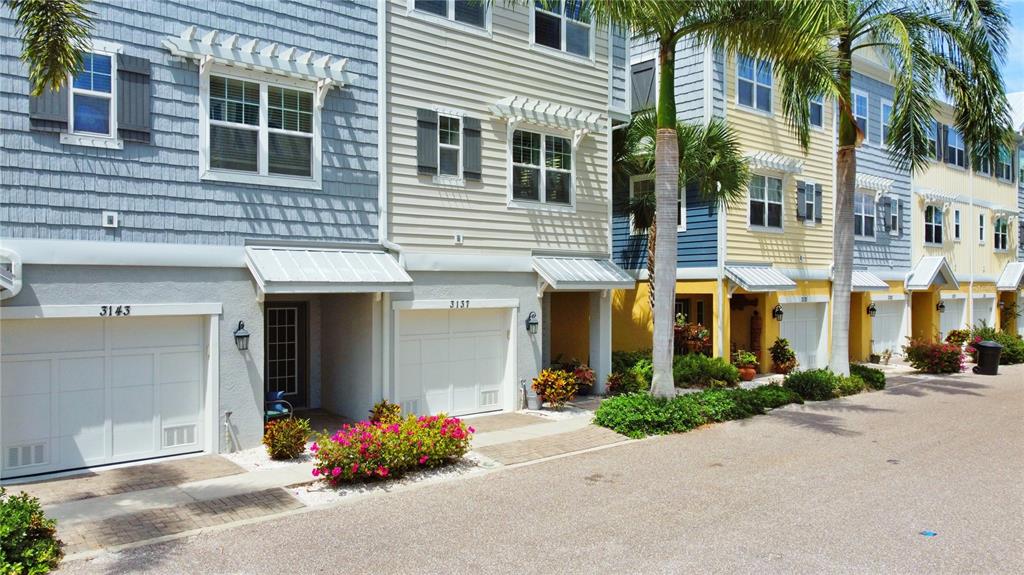 A row of multi-story townhouses with garages, colorful siding, and palm trees along a street — 3137 MOORINGS DRIVE S, ST PETERSBURG, FL