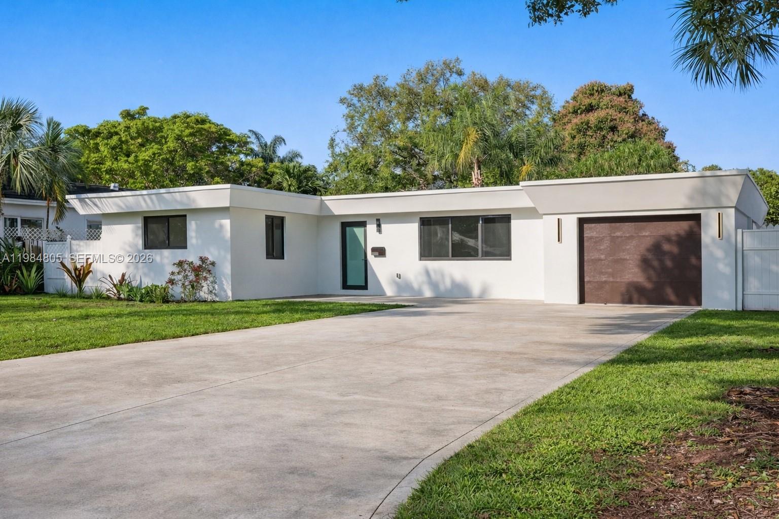 A single-story white house with a flat roof, brown garage door, and concrete driveway — 10910 NE 9th Ct, Biscayne Park FL 33161, BISCAYNE PARK, FL