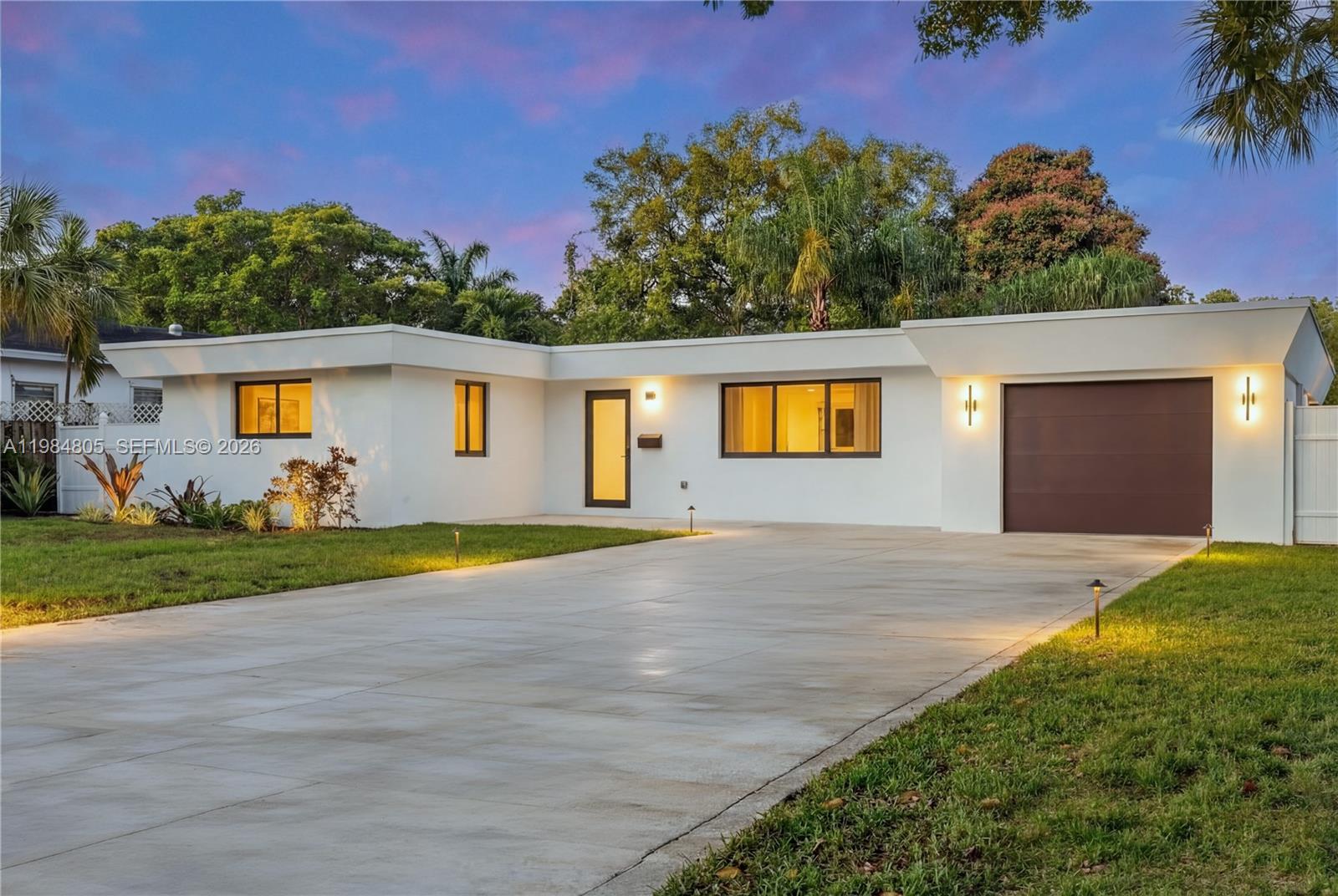 A single-story white house with a flat roof, brown garage door, and concrete driveway — 10910 NE 9th Ct, Biscayne Park FL 33161, BISCAYNE PARK, FL