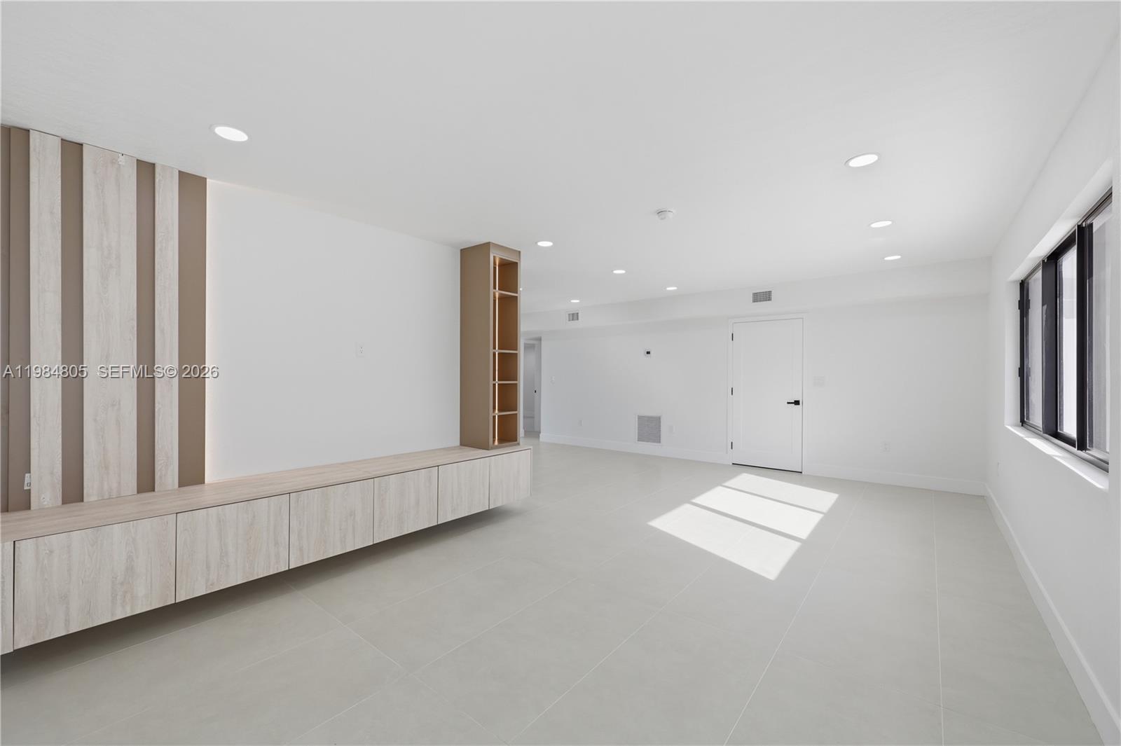 A modern, minimalist living room features light wood cabinetry, vertical wall accents, and tile flooring — 10910 NE 9th Ct, Biscayne Park FL 33161, BISCAYNE PARK, FL