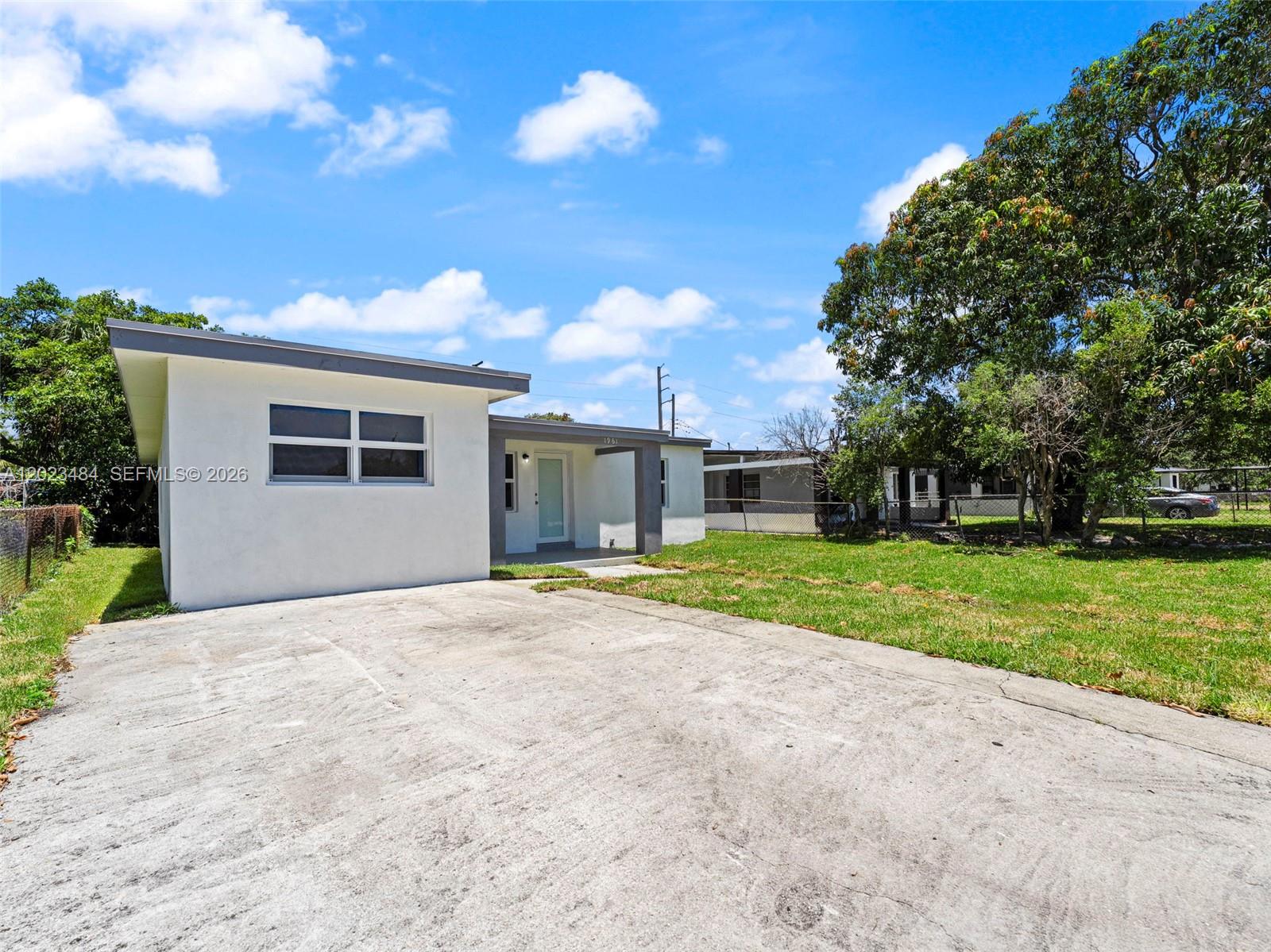 A white single-story house with a concrete driveway and a large tree in the yard — 1961 Rutland St, Opa-Locka FL 33054, OPA-LOCKA, FL